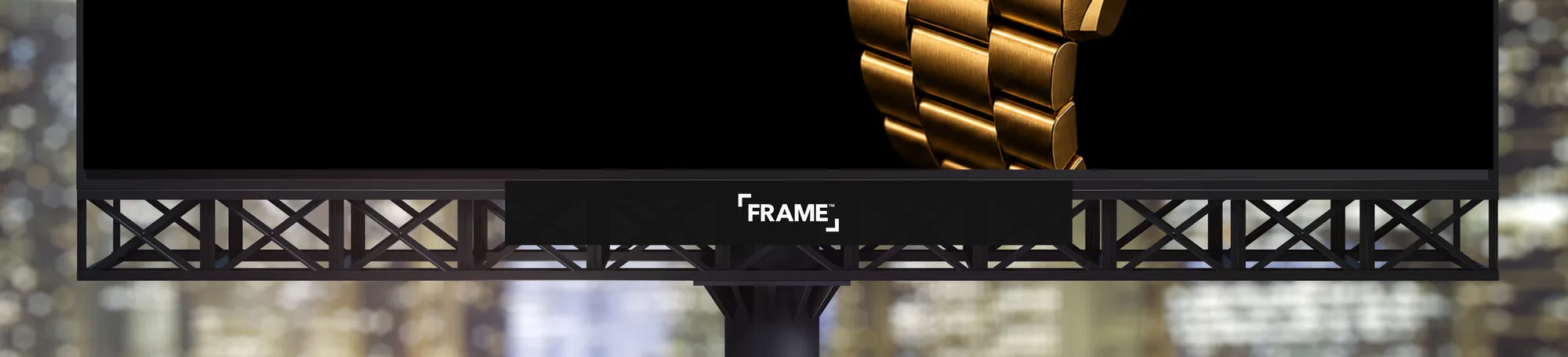 The FRAME nameplate on a black bar centered under a lit digital billboard, with the catwalk and the city behind it